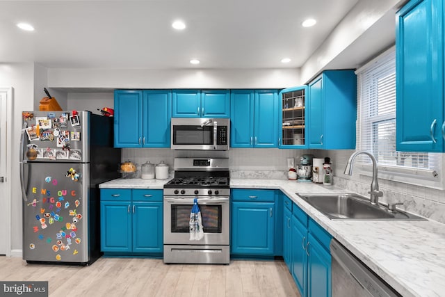 kitchen with sink, tasteful backsplash, light hardwood / wood-style flooring, blue cabinets, and appliances with stainless steel finishes