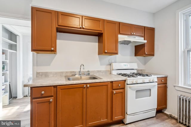 kitchen with white gas range, light hardwood / wood-style floors, radiator heating unit, and sink