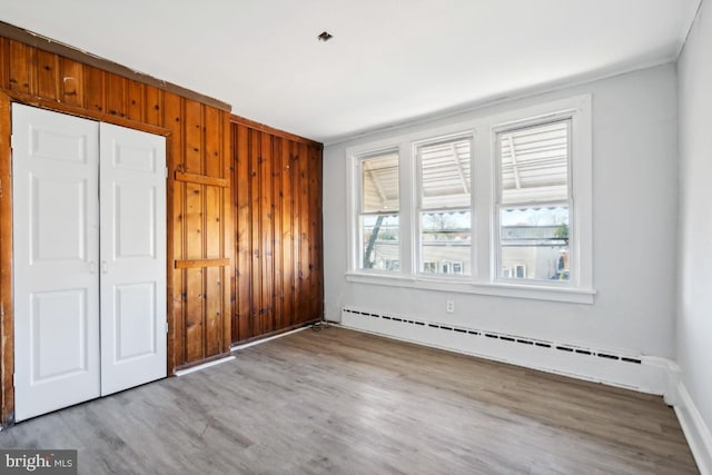 unfurnished bedroom featuring wood walls, light hardwood / wood-style floors, and baseboard heating