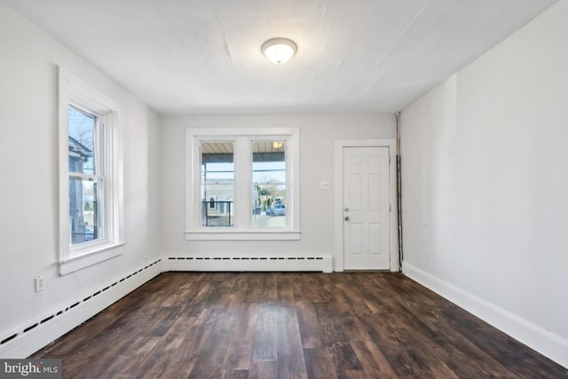 empty room featuring dark wood-type flooring, a wealth of natural light, and a baseboard heating unit