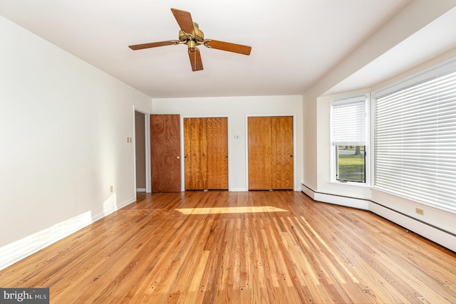 unfurnished bedroom with ceiling fan, a baseboard heating unit, light wood-type flooring, and two closets