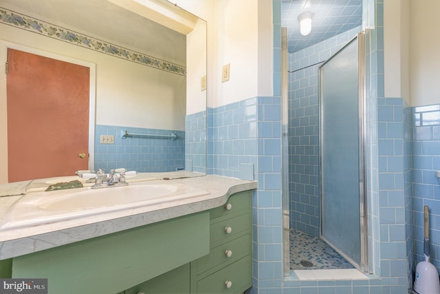 bathroom with vanity, a shower with shower door, and tile walls