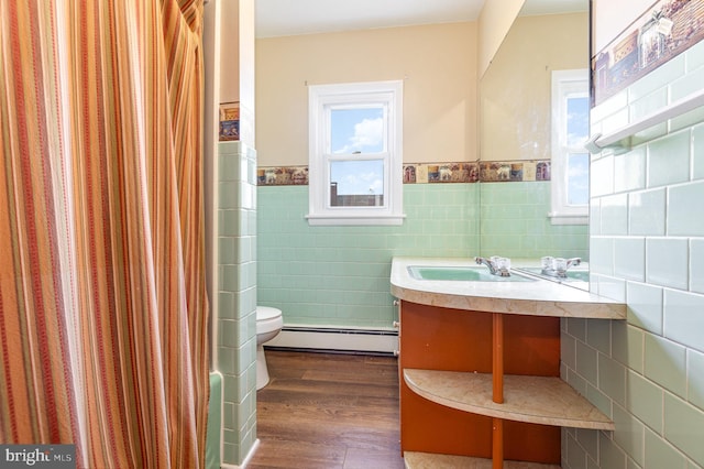 bathroom with baseboard heating, hardwood / wood-style floors, toilet, vanity, and tile walls