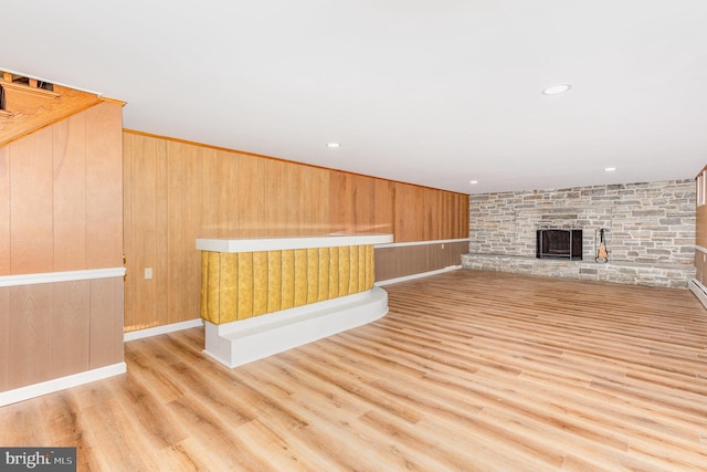 unfurnished living room featuring light wood-type flooring, a fireplace, and wooden walls