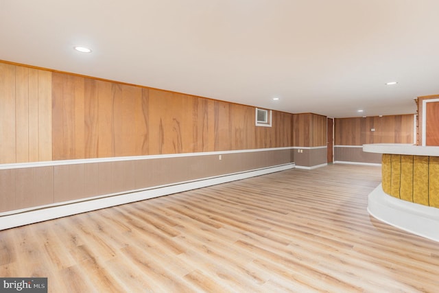 interior space with light hardwood / wood-style floors, wooden walls, and a baseboard radiator