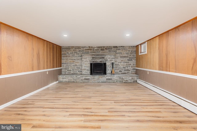 unfurnished living room with light wood-type flooring, a baseboard heating unit, and wood walls