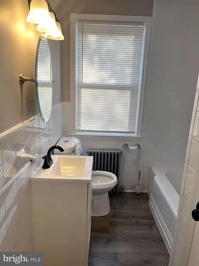 bathroom with a tub, radiator, tile walls, hardwood / wood-style floors, and vanity