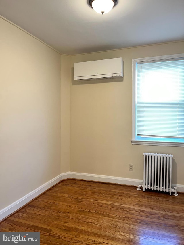 empty room with radiator, a wall unit AC, and hardwood / wood-style floors