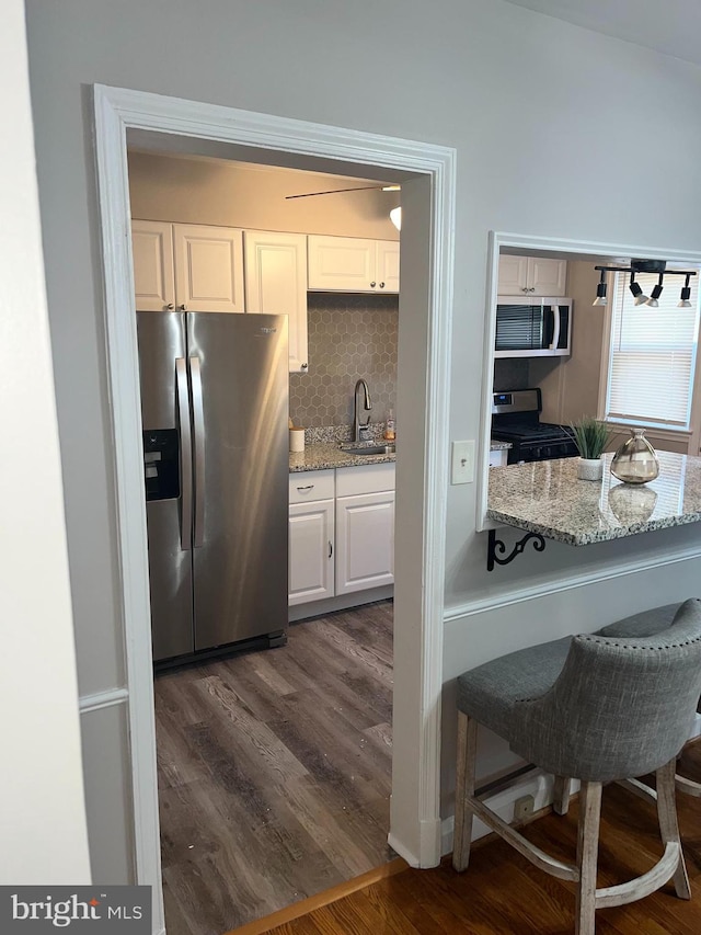 kitchen with white cabinetry, light stone countertops, appliances with stainless steel finishes, and dark hardwood / wood-style floors