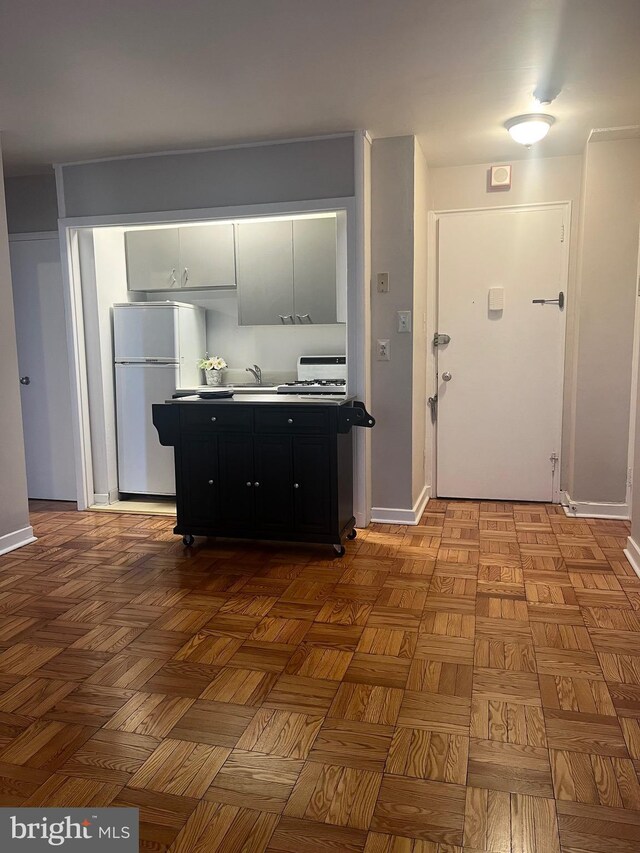 kitchen with sink, refrigerator, white cabinetry, and light parquet flooring