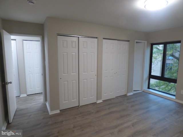 unfurnished bedroom featuring wood-type flooring, two closets, and access to outside