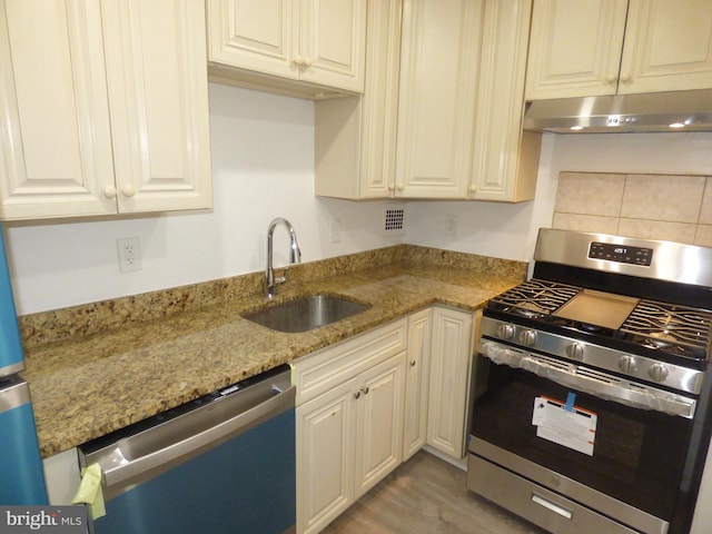 kitchen featuring light stone countertops, appliances with stainless steel finishes, sink, and light wood-type flooring