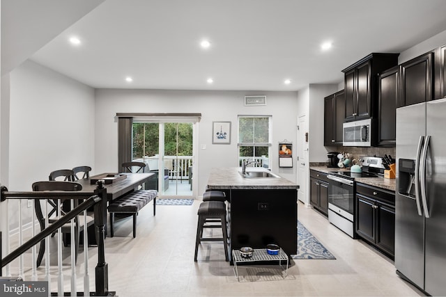 kitchen with stainless steel appliances, a center island with sink, sink, a kitchen breakfast bar, and backsplash