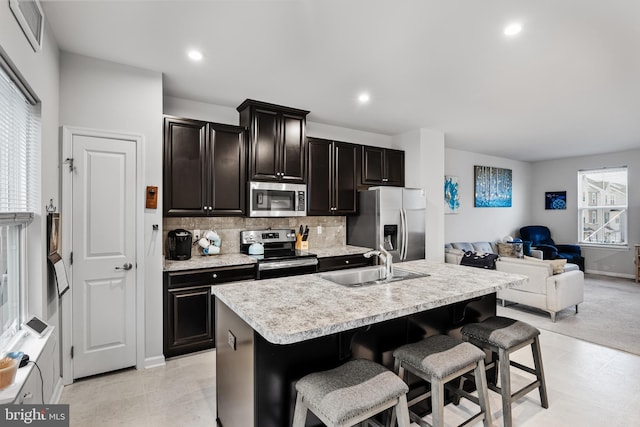 kitchen with sink, appliances with stainless steel finishes, tasteful backsplash, a breakfast bar area, and a kitchen island with sink