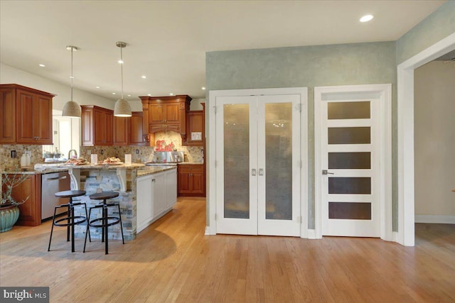 kitchen with pendant lighting, dishwasher, a center island, a kitchen breakfast bar, and light stone counters