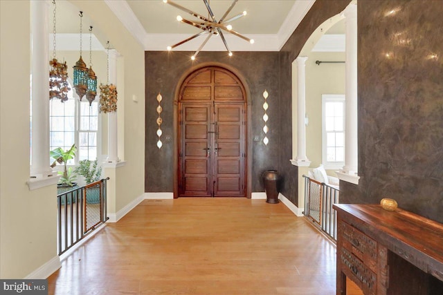 foyer entrance with arched walkways, a chandelier, wood finished floors, ornamental molding, and baseboards