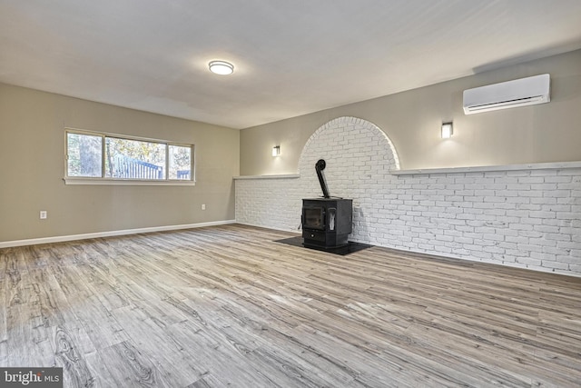 unfurnished living room with light wood-type flooring, a wall unit AC, brick wall, and a wood stove