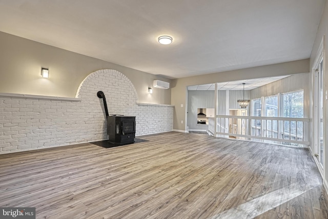 unfurnished living room with hardwood / wood-style floors, a wall unit AC, brick wall, and a wood stove