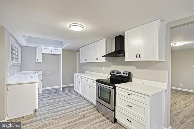 kitchen with stainless steel electric range, wall chimney exhaust hood, and white cabinets