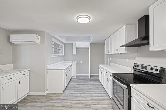 kitchen with a wall unit AC, stainless steel electric range, light hardwood / wood-style flooring, white cabinets, and wall chimney range hood