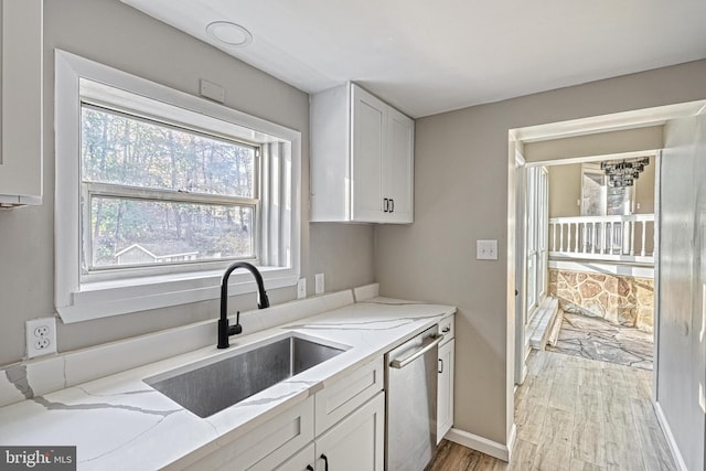 kitchen with sink, stainless steel dishwasher, light stone countertops, white cabinetry, and light hardwood / wood-style flooring