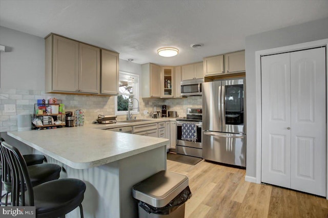 kitchen featuring appliances with stainless steel finishes, sink, a breakfast bar area, kitchen peninsula, and light wood-type flooring