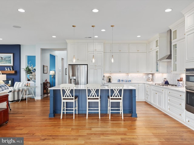 kitchen featuring a kitchen island with sink, light hardwood / wood-style flooring, hanging light fixtures, and appliances with stainless steel finishes