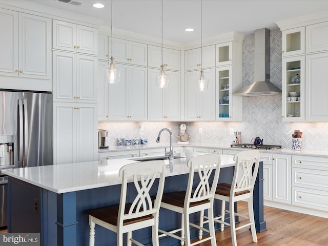 kitchen featuring a center island with sink, backsplash, wall chimney range hood, and stainless steel appliances