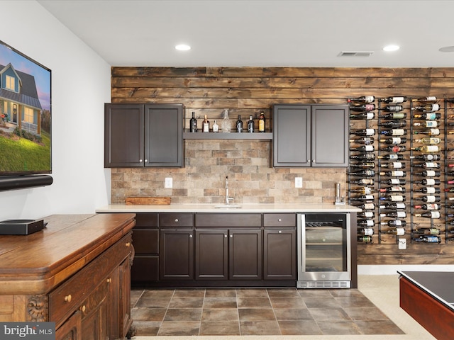 bar featuring dark brown cabinets, sink, wine cooler, and tasteful backsplash