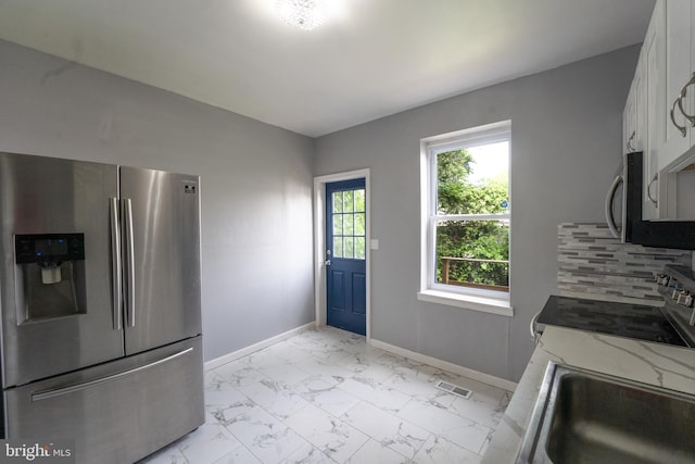 kitchen featuring stainless steel appliances, white cabinetry, sink, light stone counters, and decorative backsplash