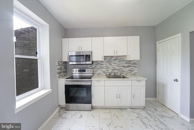 kitchen with stainless steel appliances, white cabinetry, sink, and backsplash