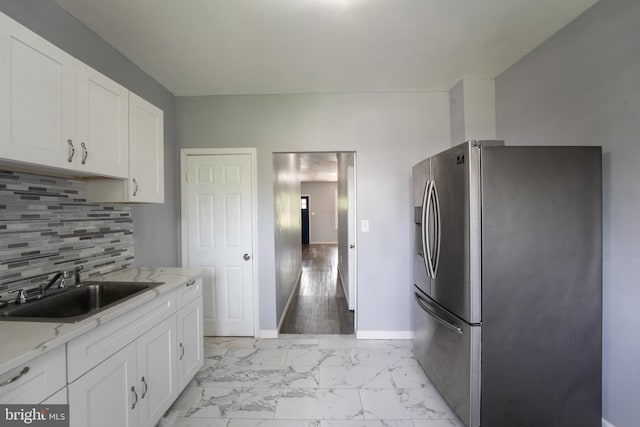 kitchen with light hardwood / wood-style floors, white cabinetry, sink, light stone countertops, and stainless steel fridge