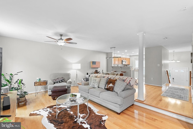 living room with light hardwood / wood-style floors, ceiling fan, and decorative columns