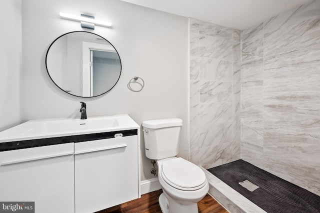 bathroom with hardwood / wood-style floors, vanity, toilet, and tiled shower