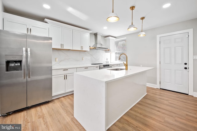 kitchen featuring stainless steel appliances, wall chimney exhaust hood, decorative light fixtures, light hardwood / wood-style flooring, and white cabinets