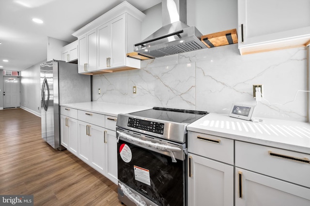 kitchen featuring wood-type flooring, white cabinetry, wall chimney range hood, appliances with stainless steel finishes, and decorative backsplash