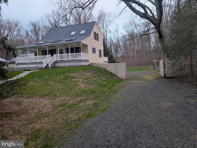 rear view of house featuring a lawn, gravel driveway, a chimney, a shingled roof, and a porch