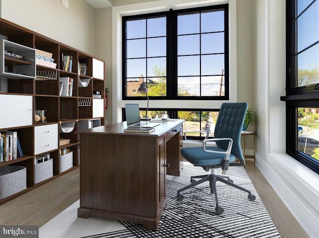 home office with healthy amount of natural light, light wood-style flooring, baseboards, and a towering ceiling