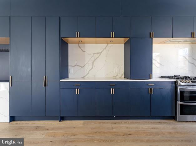 kitchen featuring double oven range, blue cabinets, light wood-style flooring, decorative backsplash, and light countertops