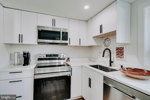 kitchen featuring stainless steel appliances, a sink, white cabinets, recessed lighting, and light stone countertops