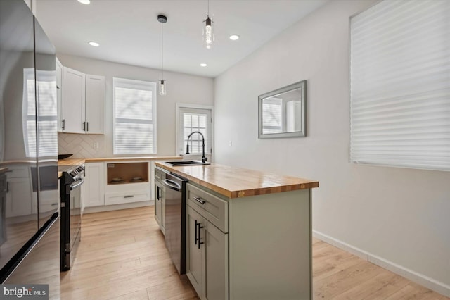 kitchen featuring butcher block counters, appliances with stainless steel finishes, pendant lighting, sink, and an island with sink