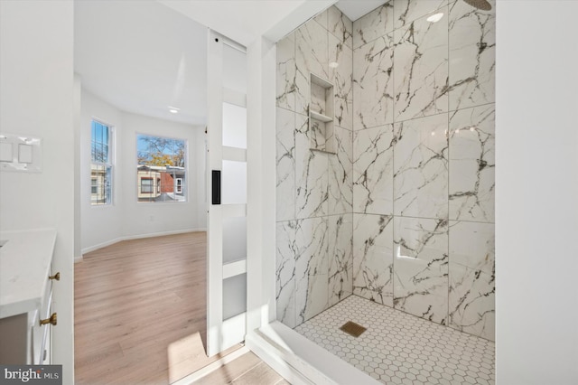 bathroom with wood-type flooring, a tile shower, and vanity