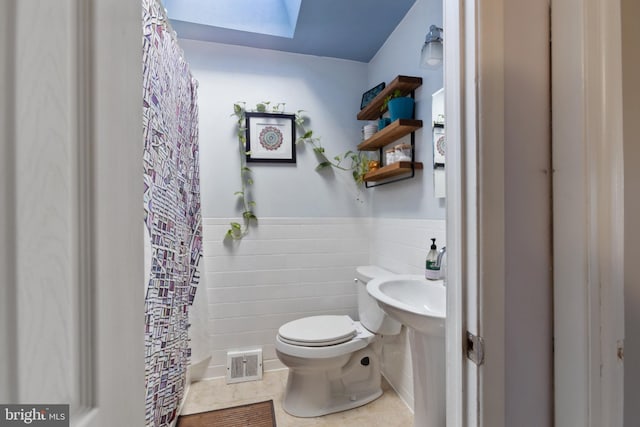 bathroom with tile walls, tile patterned flooring, a skylight, and toilet