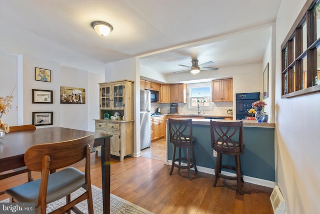 kitchen with light hardwood / wood-style floors, sink, black appliances, kitchen peninsula, and tasteful backsplash