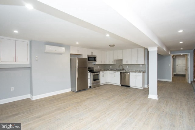 kitchen with appliances with stainless steel finishes, tasteful backsplash, a wall unit AC, white cabinets, and light wood-type flooring