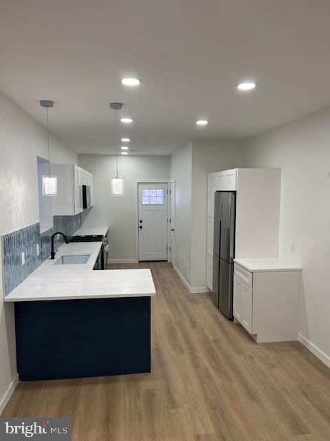 kitchen featuring kitchen peninsula, light wood-type flooring, sink, decorative light fixtures, and white cabinets