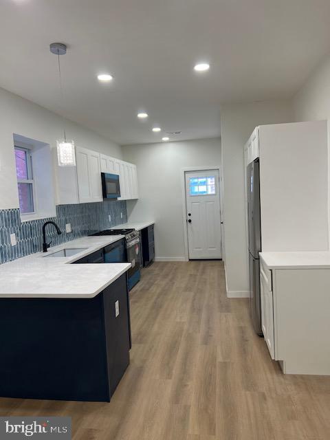 kitchen featuring white cabinetry, sink, tasteful backsplash, pendant lighting, and light wood-type flooring