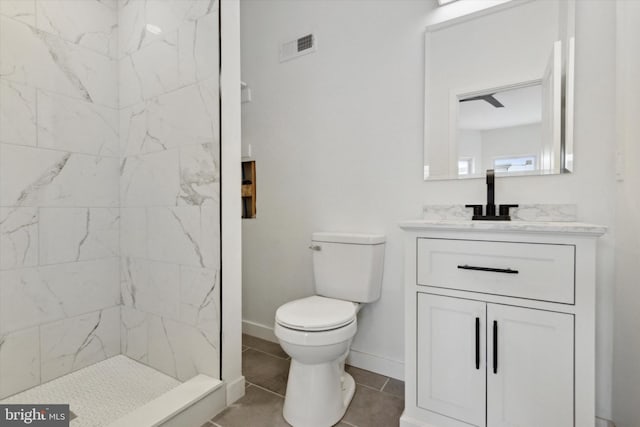 bathroom with tile patterned flooring, vanity, toilet, and a tile shower