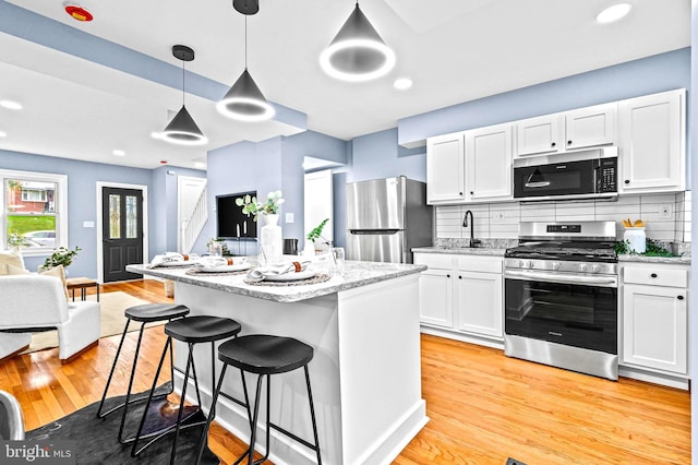 kitchen with white cabinetry, stainless steel appliances, tasteful backsplash, light hardwood / wood-style flooring, and decorative light fixtures