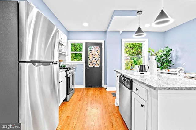 kitchen featuring light stone countertops, light wood-type flooring, stainless steel appliances, white cabinetry, and hanging light fixtures